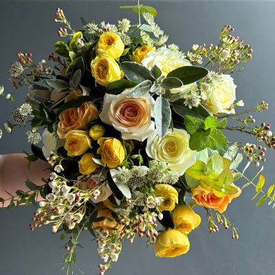 Elegant hand-tied bouquet featuring peach, white, and spray roses with seasonal fillers in soft yellow and ivory tones.